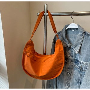 Gros plan d'un sac demi-lune en nylon orange vif avec détails de poche sur un cintre