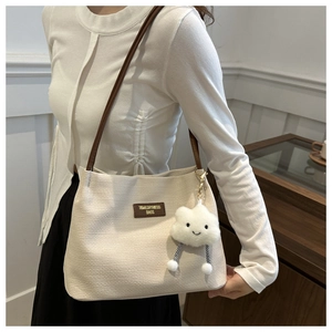 Detail of cream woven shoulder bag with brown leather strap and plush cloud charm