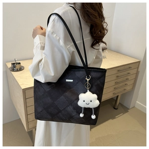 Close-up of black quilted tote bag with cute white cloud plush charm and metal plaque