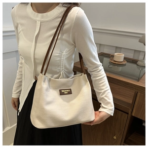 Close-up of beige woven bucket bag with leather brand tag and thin brown shoulder straps