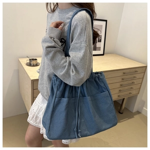 Detail of blue denim bucket bag with drawstring closure and large exterior pockets