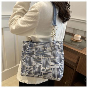 Detail of blue striped canvas tote bag with leather logo patch and gold chain strap