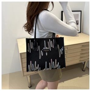 Detail of black tote bag with colorful wave embroidery and metal logo plate on shoulder