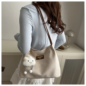 Detail of waffle textured beige bucket bag with brown leather strap and plush cloud charm