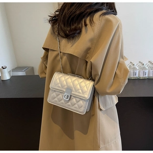 Close-up of silver quilted chain shoulder bag with metallic clasp worn with a trench coat