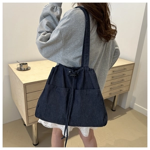 Detailed back view of model wearing large denim drawstring bucket bag with pockets