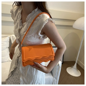Detail of bright orange crossbody bag with unique wavy scalloped edge flap design