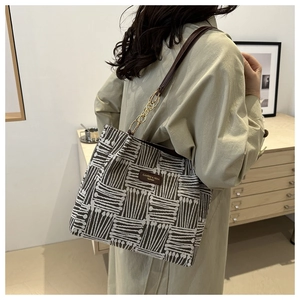 Detail of a brown woven pattern tote bag with gold chain and leather label on a model