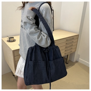 Detail of dark blue denim bucket bag featuring dual front pockets and drawstring closure
