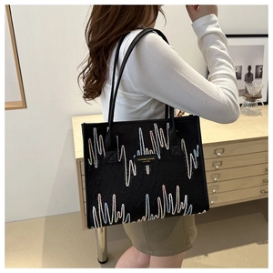 Detail of black tote bag with colorful wave embroidery and leather logo tag on a shoulder strap