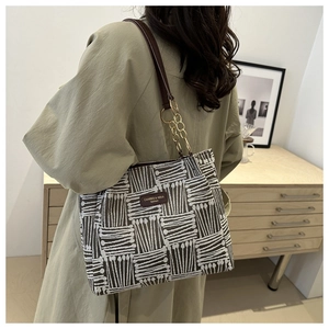 Detail of woven lattice pattern handbag with dark brown leather strap and metal chain links
