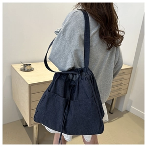 Deep blue denim drawstring bucket bag with large pockets shown on shoulder model