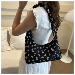 Detail of printed fabric shoulder bag with white bows and pleated strap on model