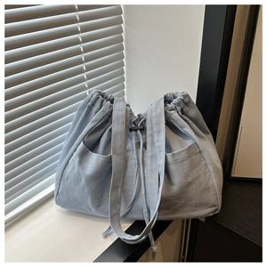 Detail of light blue denim tote bag with drawstring closure and front large pocket
