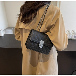 Detail of a black quilted crossbody bag with a silver chain strap shown worn by a model