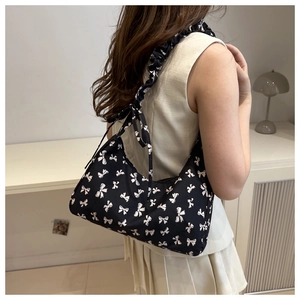 Detail of black shoulder bag with white bow patterns and ruffled strap on a model