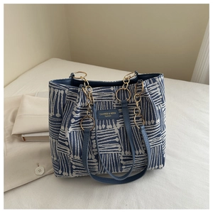 Detail of blue striped woven tote bag with leather logo patch and gold chain strap