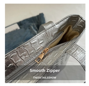 Detail of a gold metal zipper on a silver crocodile pattern tote bag with beige lining