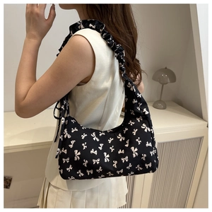 Close-up of black floral shoulder bag featuring ruffle straps and white bow pattern