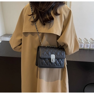 Detail of black quilted leather shoulder bag with metal chain strap and twist-lock closure