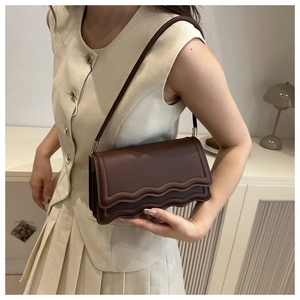 Detail view of dark brown leather crossbody bag with unique triple wavy flap design