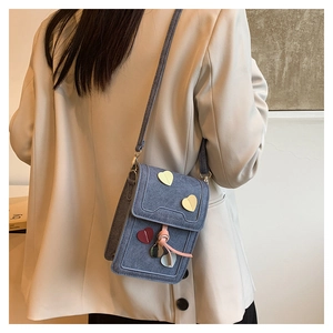 Detail of denim crossbody phone bag featuring colorful heart patches and pink tassels