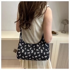 Detailed view of black canvas shoulder bag with white bow pattern on female model back