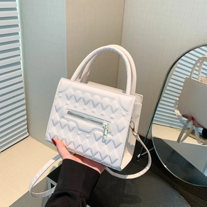 White quilted crossbody bag with diamond pattern, handheld style in front of a mirror
