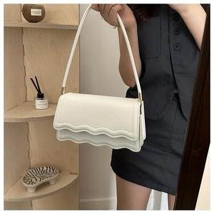 Détail du sac à bandoulière blanc avec rabat à bords ondulés et finitions métalliques dorées