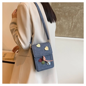 Close-up of a blue denim crossbody phone bag with heart patches on a white blazer