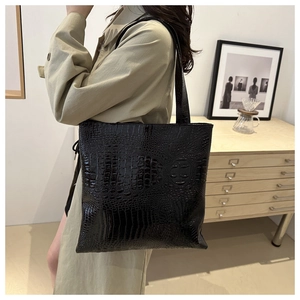 Detail showing high-quality black crocodile embossed leather texture on a tote bag
