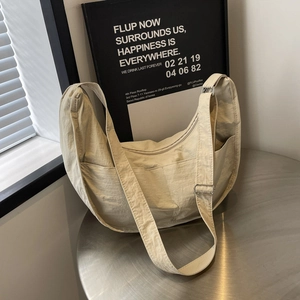 Sac bandoulière minimaliste en nylon beige en forme de croissant sur une table en métal