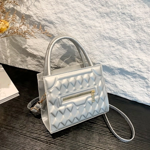 Silver quilted crossbody bag with gold zipper detail on stone background