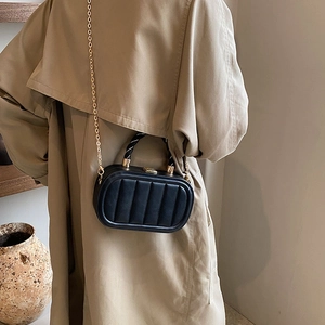 Vertical quilted black square handbag with gold chain strap carried with a trench coat
