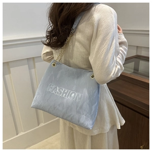 Detail of light blue tote bag with FASHION embossed texture and gold chain strap