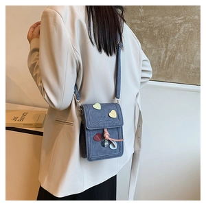 Detail of blue denim shoulder bag featuring colorful heart patches and pink drawstring charm