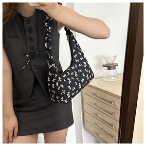 Detailed close-up of a black canvas bag with white bow patterns and ruffled strap design