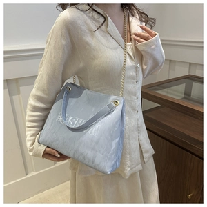 Detail of light blue pleated tote bag featuring embossed FASHION text and gold chain