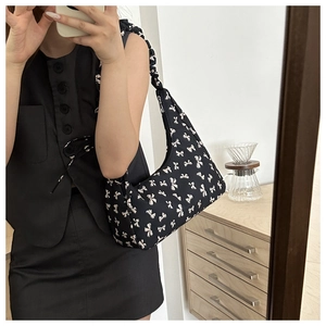 Detail of black underarm bag with white bow pattern and ruched shoulder strap