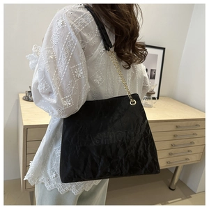 Detail of black tote bag featuring ruched texture and golden chain strap for daily wear
