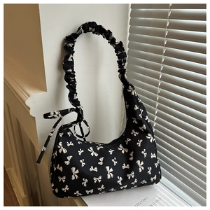 Close-up of black canvas shoulder bag featuring white bow patterns and pleated straps