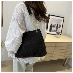 Detail of black tote bag with FASHION embossing and gold chain leather strap on a model
