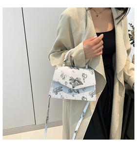 Detail of white butterfly print handbag featuring a silver bow metal buckle and adjustable strap