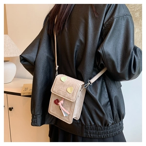 Close-up of beige canvas crossbody bag with colorful heart patches and ribbon on a model