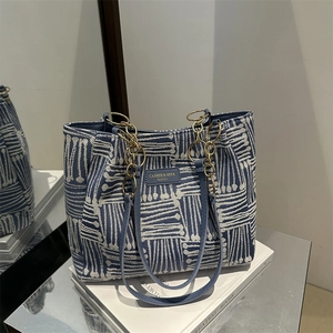 Blue and white woven tote bag with leather straps and gold chain on a minimalist background