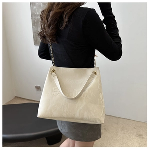 Detail of cream tote bag featuring 3D FASHION embossing and gold chain shoulder strap