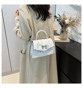 Détail d'un sac à bandoulière blanc avec imprimé papillon vert et boucle nœud argenté