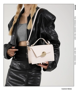 Detail of cream crossbody bag featuring a unique gold pebble clasp and adjustable strap