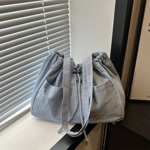 Large denim drawstring bucket bag with side pockets and casual style shown in a studio