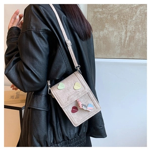 Detail of crossbody bag with colorful heart patches and pink bow on a leather jacket